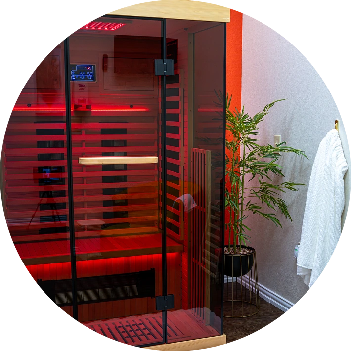 Red light therapy sauna cabin with glass doors, control panel, and decorative plant in wellness spa