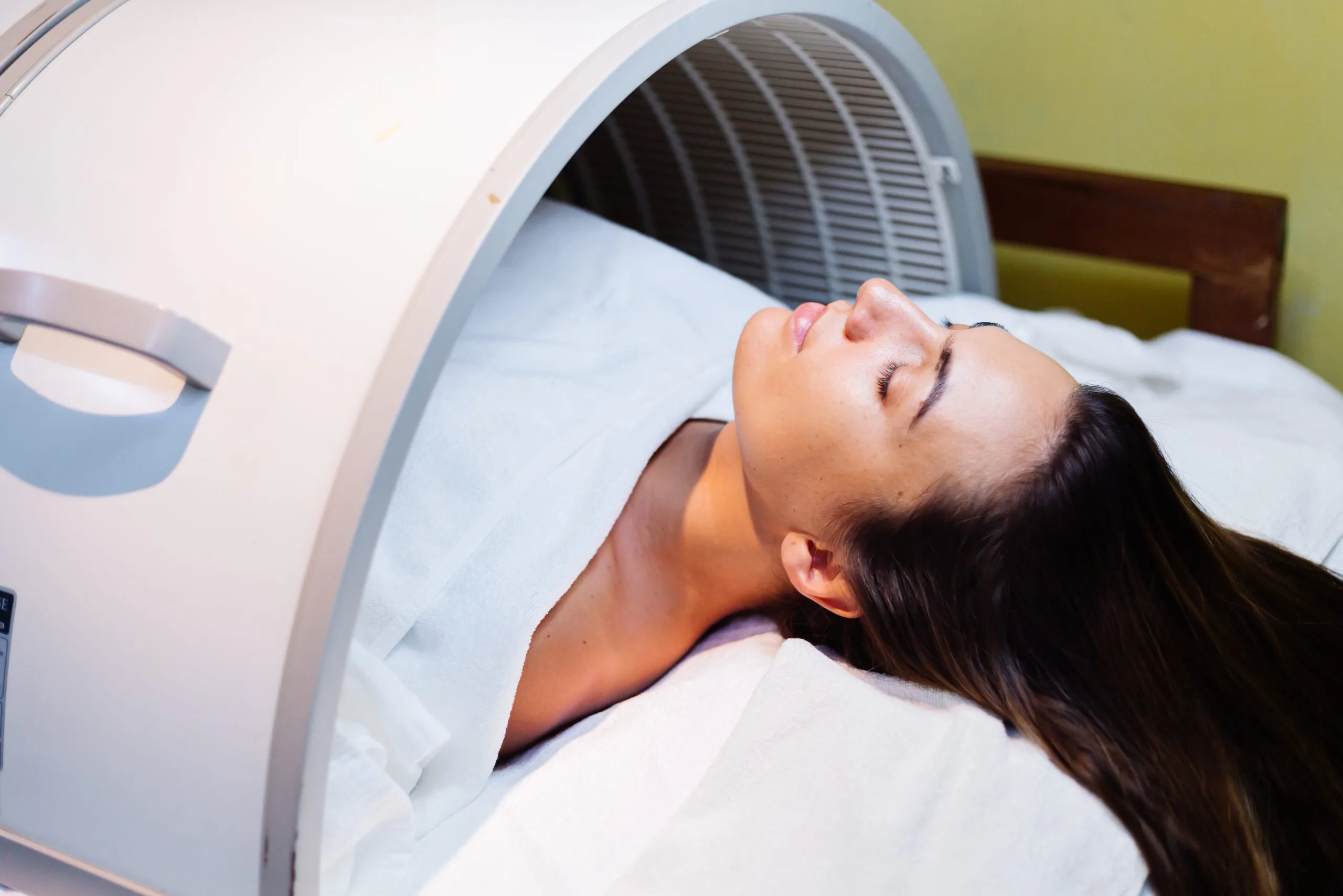 Woman lying on treatment table receiving LED light therapy facial rejuvenation procedure